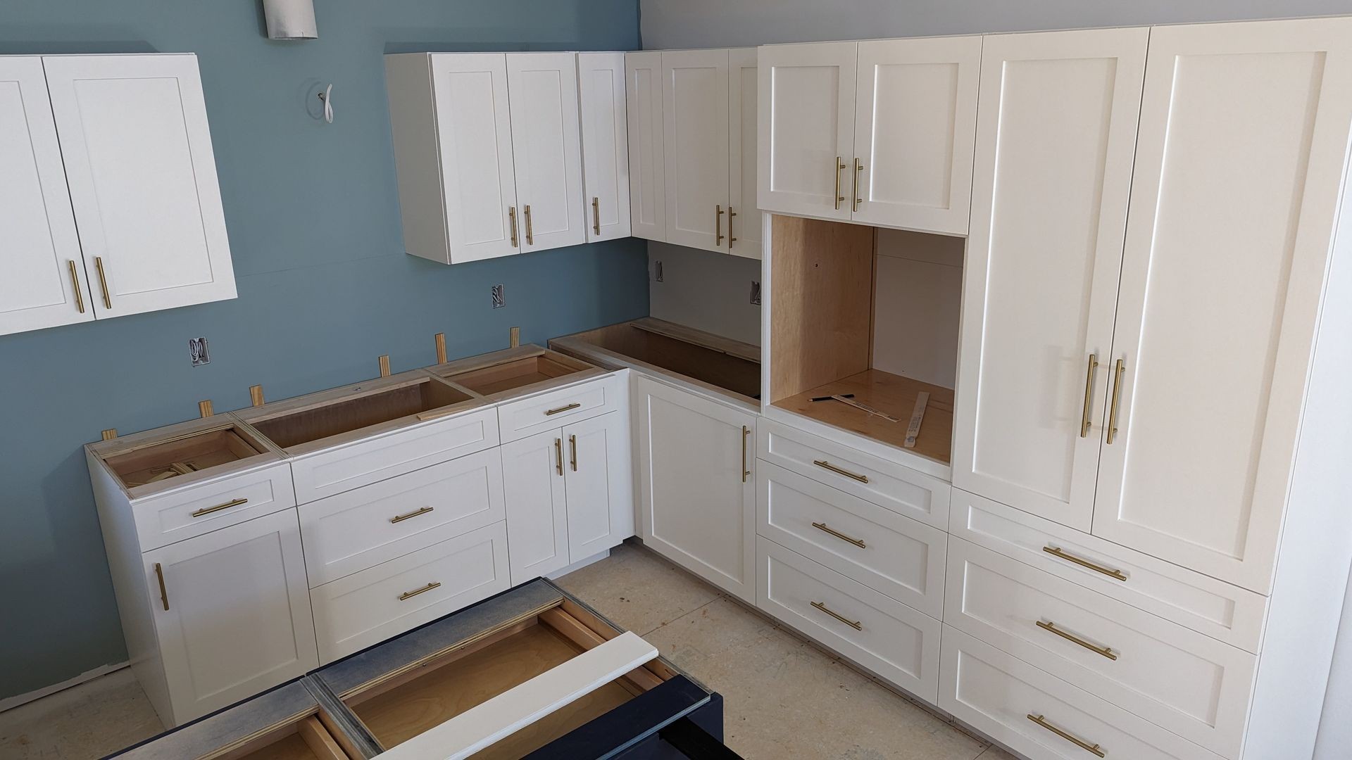 Partial kitchen installation with white cabinets and gold handles against a blue wall.